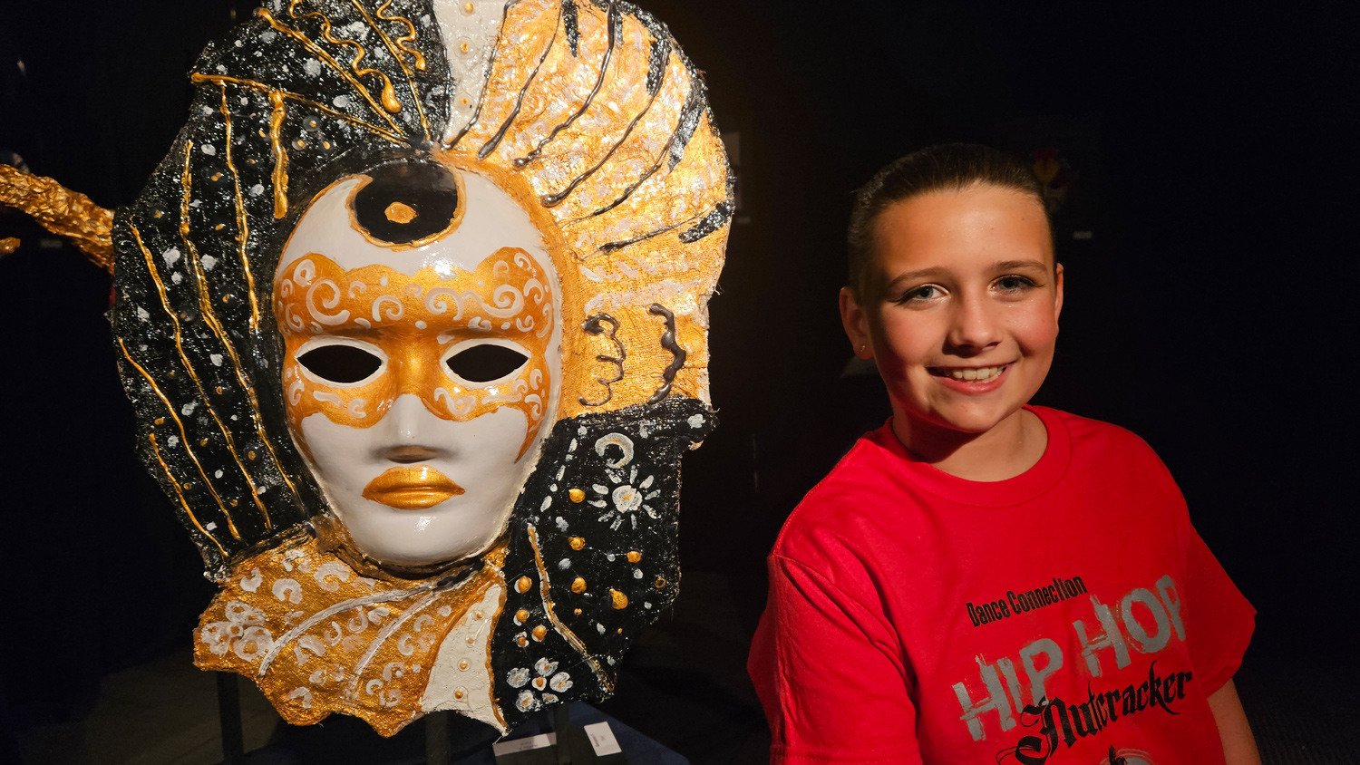 7th Grade student stands proudly by the mask she created for Arts Night