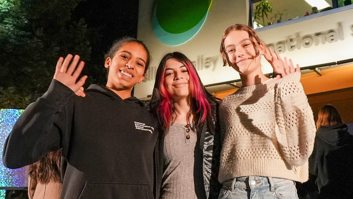 Three 9th Graders wave to the camera at the front of the school