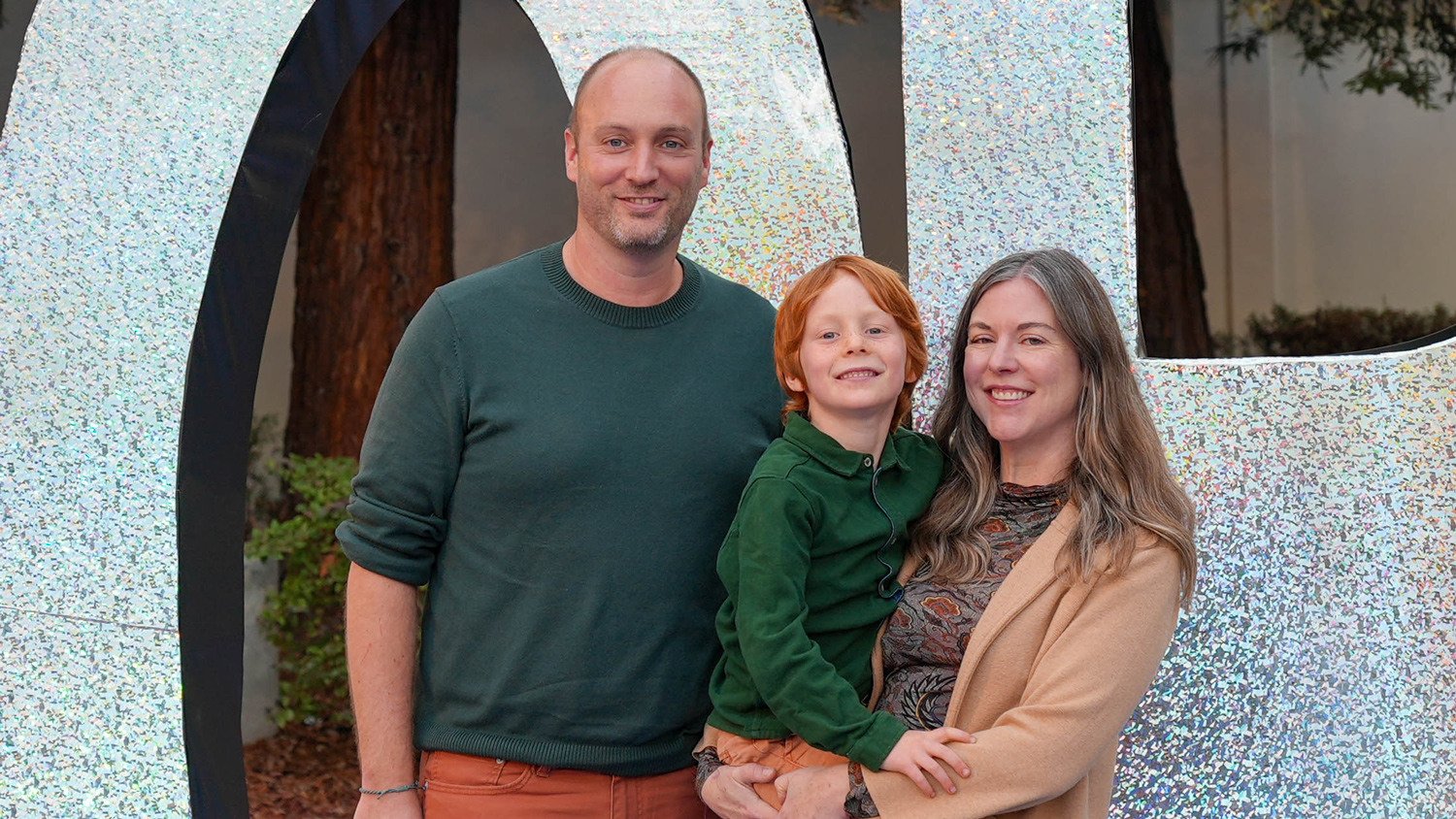 Parents and their child pose in front of the glittery One World signage