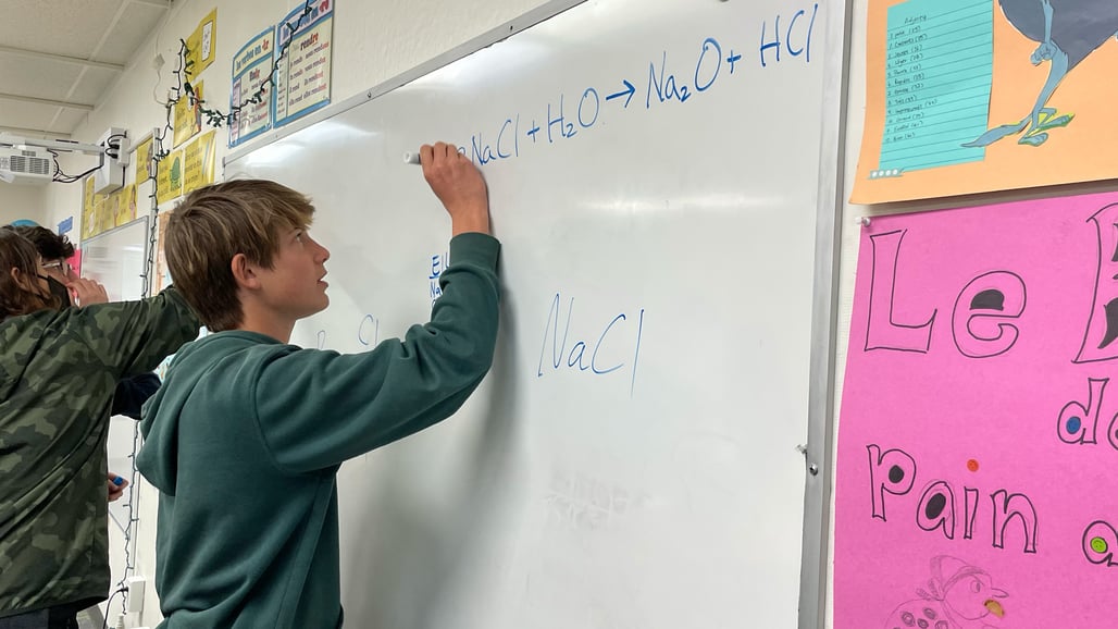 10th Grader working on a chemical equation on the white board.