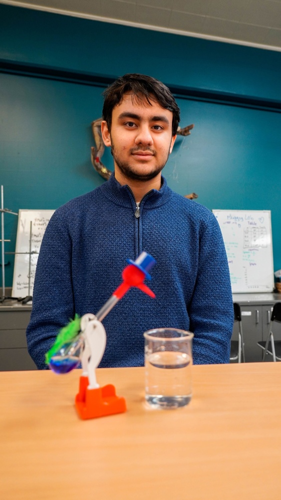 Marselis S. posing in front of his drinking bird as part of his research project in 12 Grade.