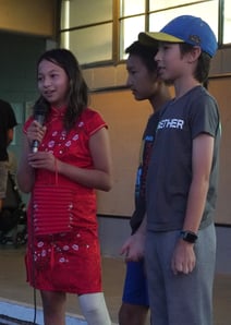 Fang Xi Cheng, Paxton Cunningham, and Ethan Jiang recite poetry and stories in front of the crowd. 