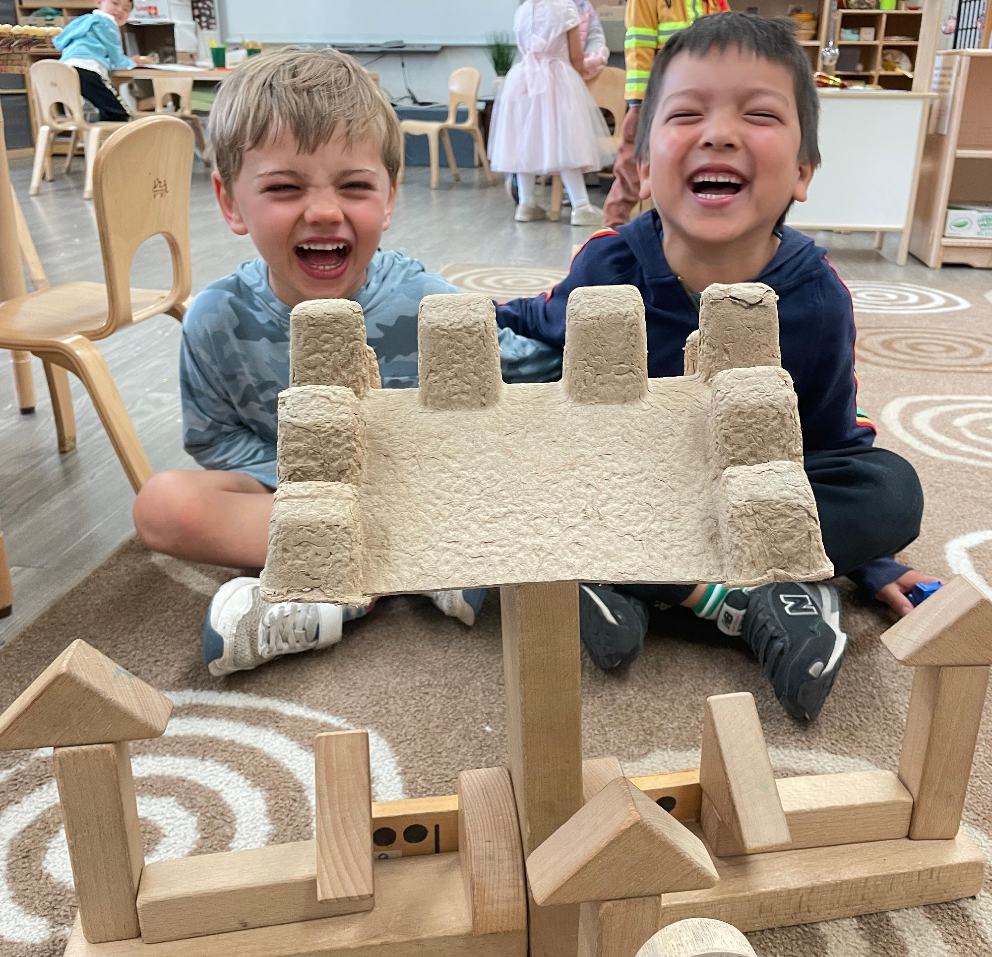 Two Early Years students building a castle out of wooden blocks and a box carton.