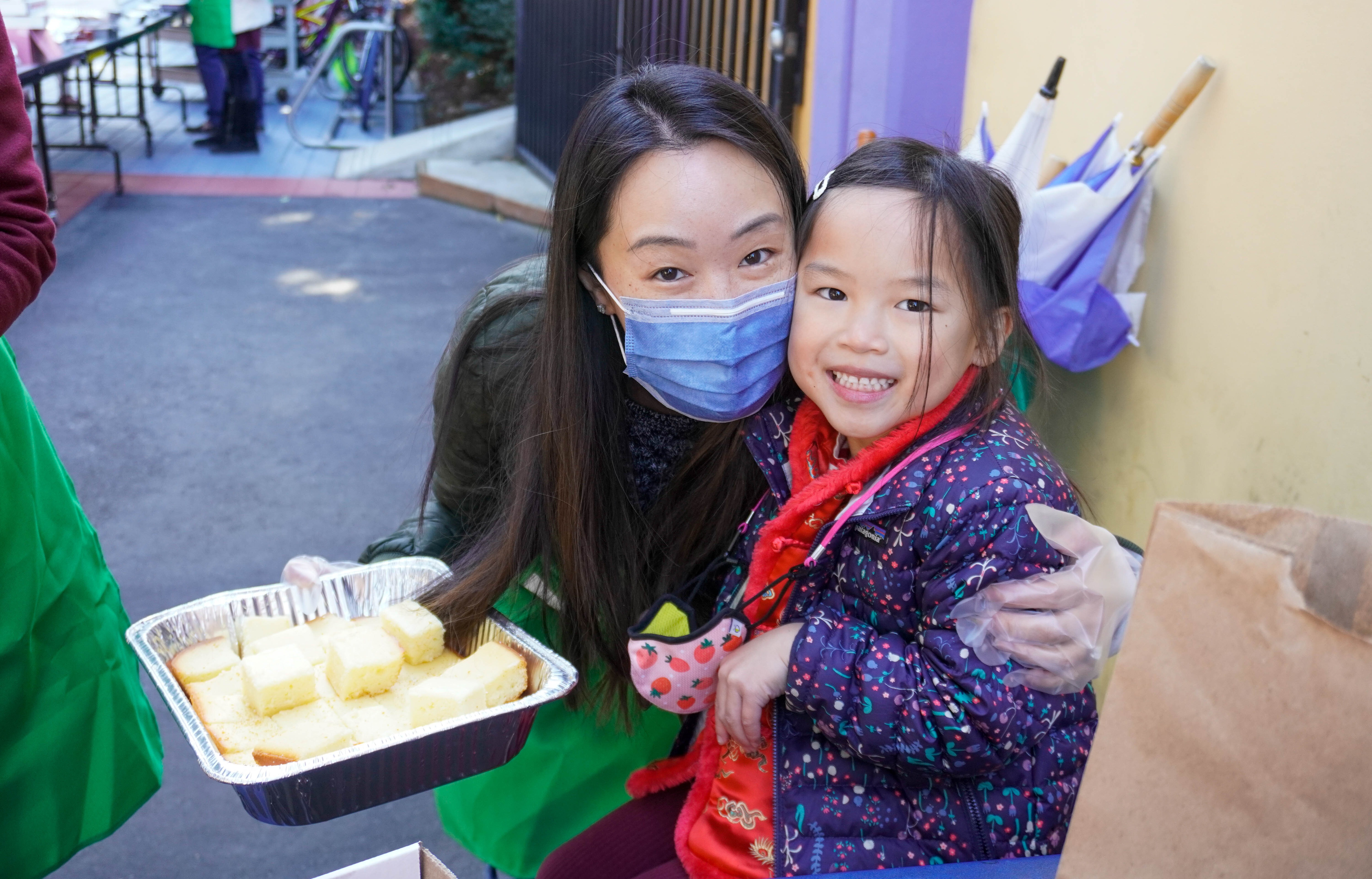 A volunteer mom holding a tray of nian gao giving her daughter a hug.