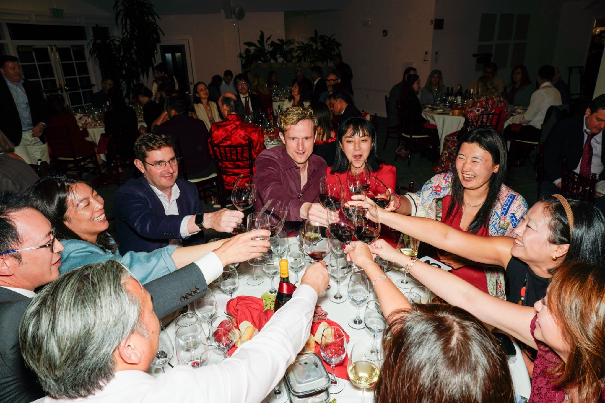 A table of 10 cheers their wine glasses together at the middle of their table