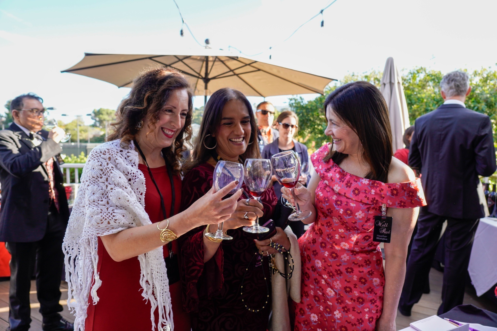 Three women cheers and clink their wine glasses together outside at SDV