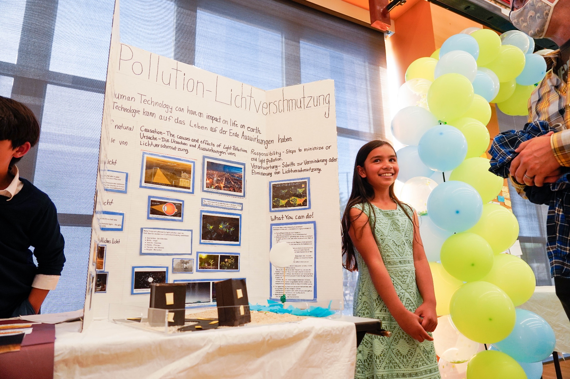 German 5th graders standing next to her project about the effects of technology on pollution.